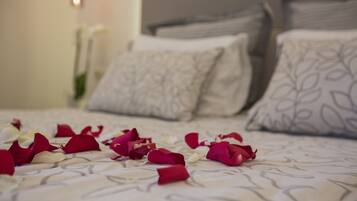 Una cama con pétalos de rosa esparcidos sobre el edredón, almohadas con estampado de hojas y una lámpara de pared.