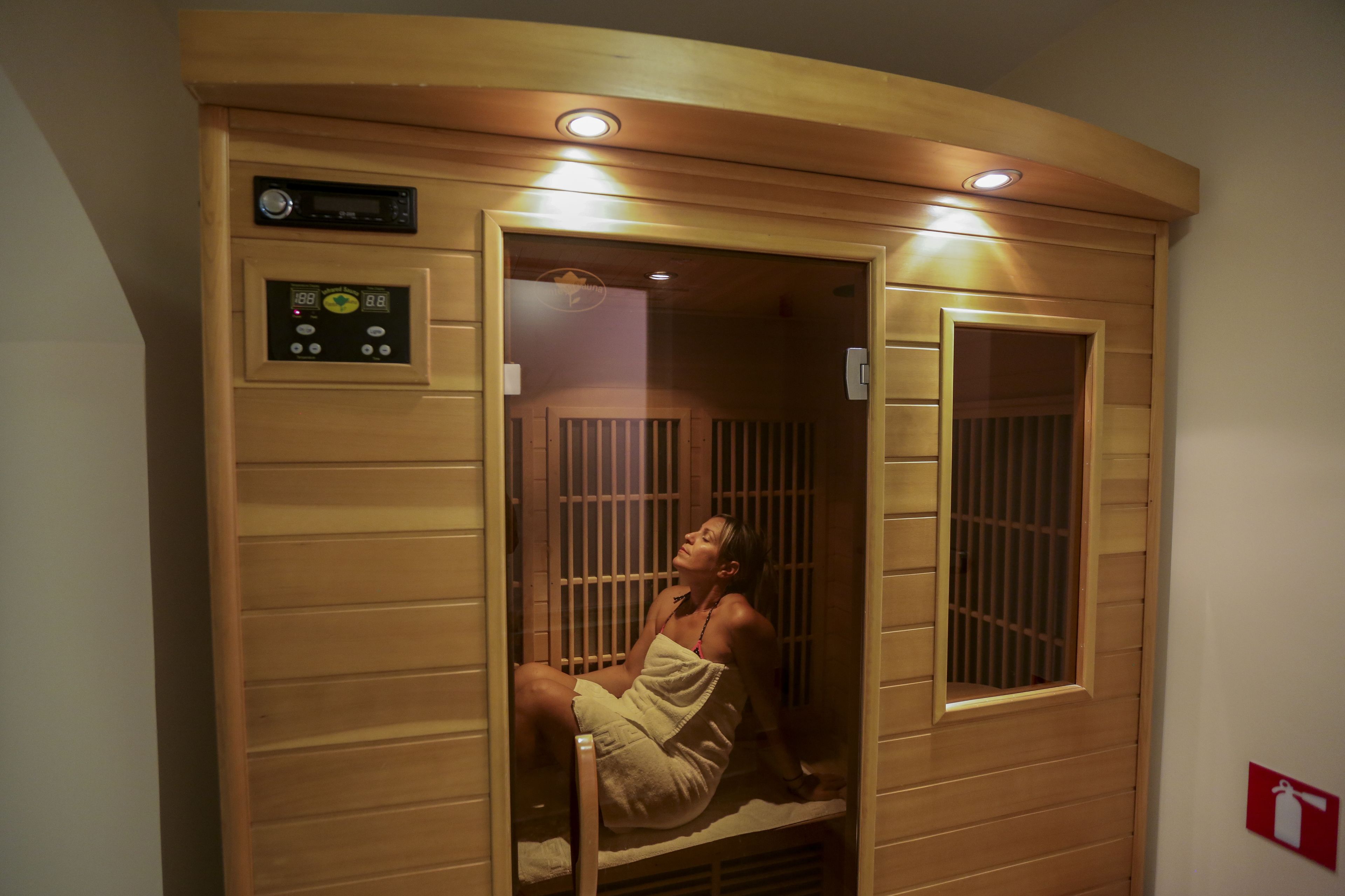 A sauna room with a control panel, wooden walls, and a window.