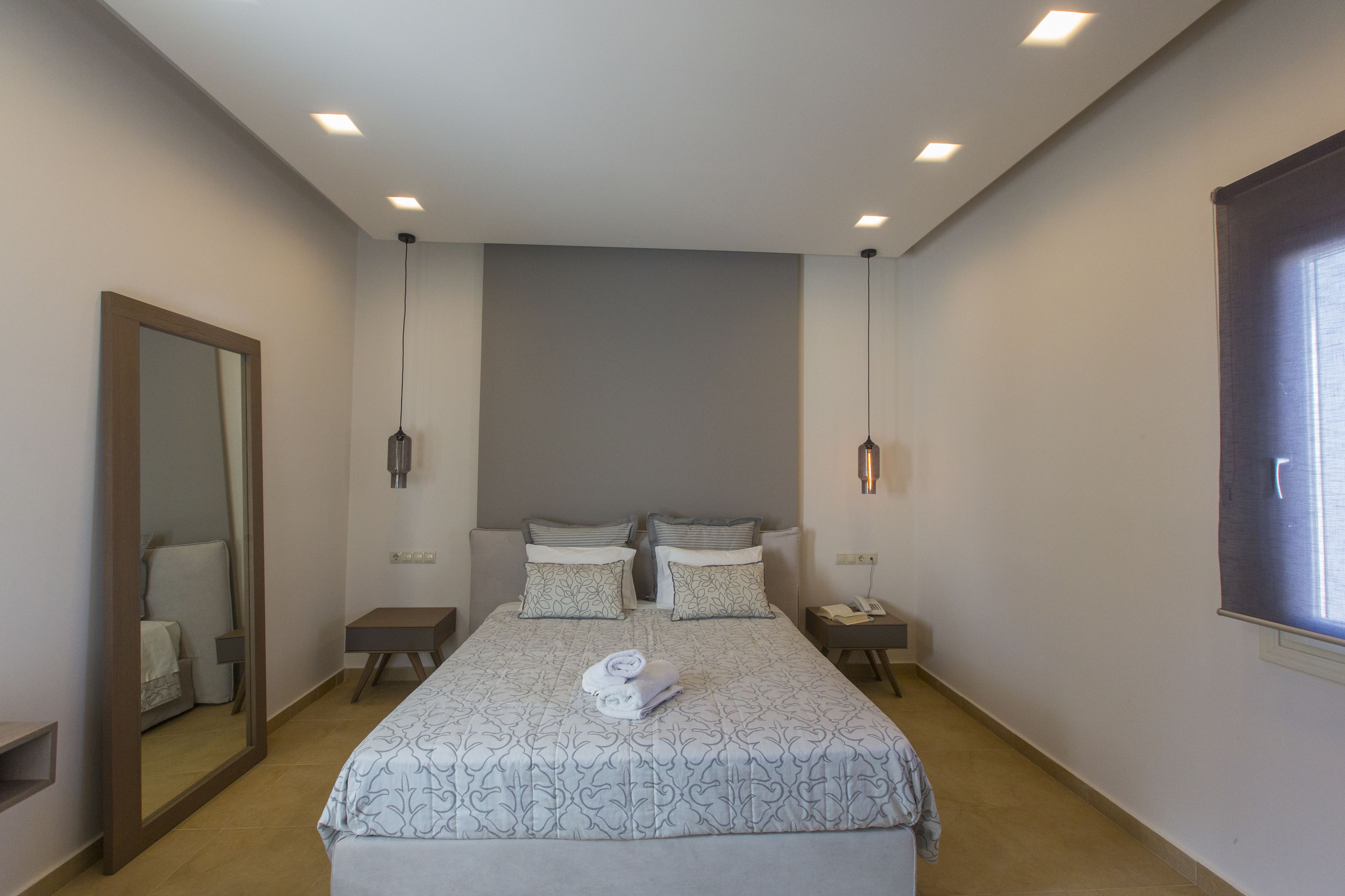 A modern hotel room with a large bed, two bedside tables, a mirror, and a window.