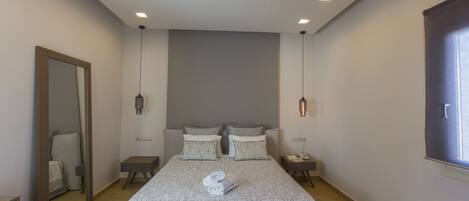 A modern hotel room with a large bed, two bedside tables, a mirror, and a window.
