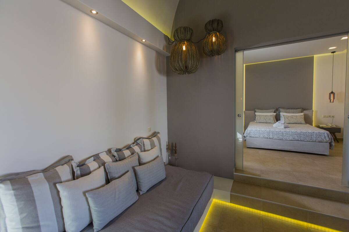 A modern bedroom with a large bed, a sofa, and a mirror reflecting the room.