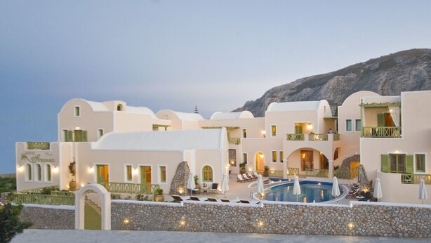 A hotel with multiple buildings, a swimming pool, and a mountainous backdrop. - Hotel Anassa (Santorini)