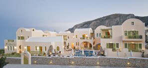 A hotel with multiple buildings, a swimming pool, and a mountainous backdrop. - Hotel Anassa (Santorini)