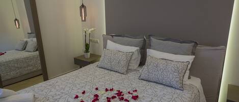 A neatly made bed with patterned bedding and pillows, a bedside table with a vase of flowers, and a mirror on the wall.