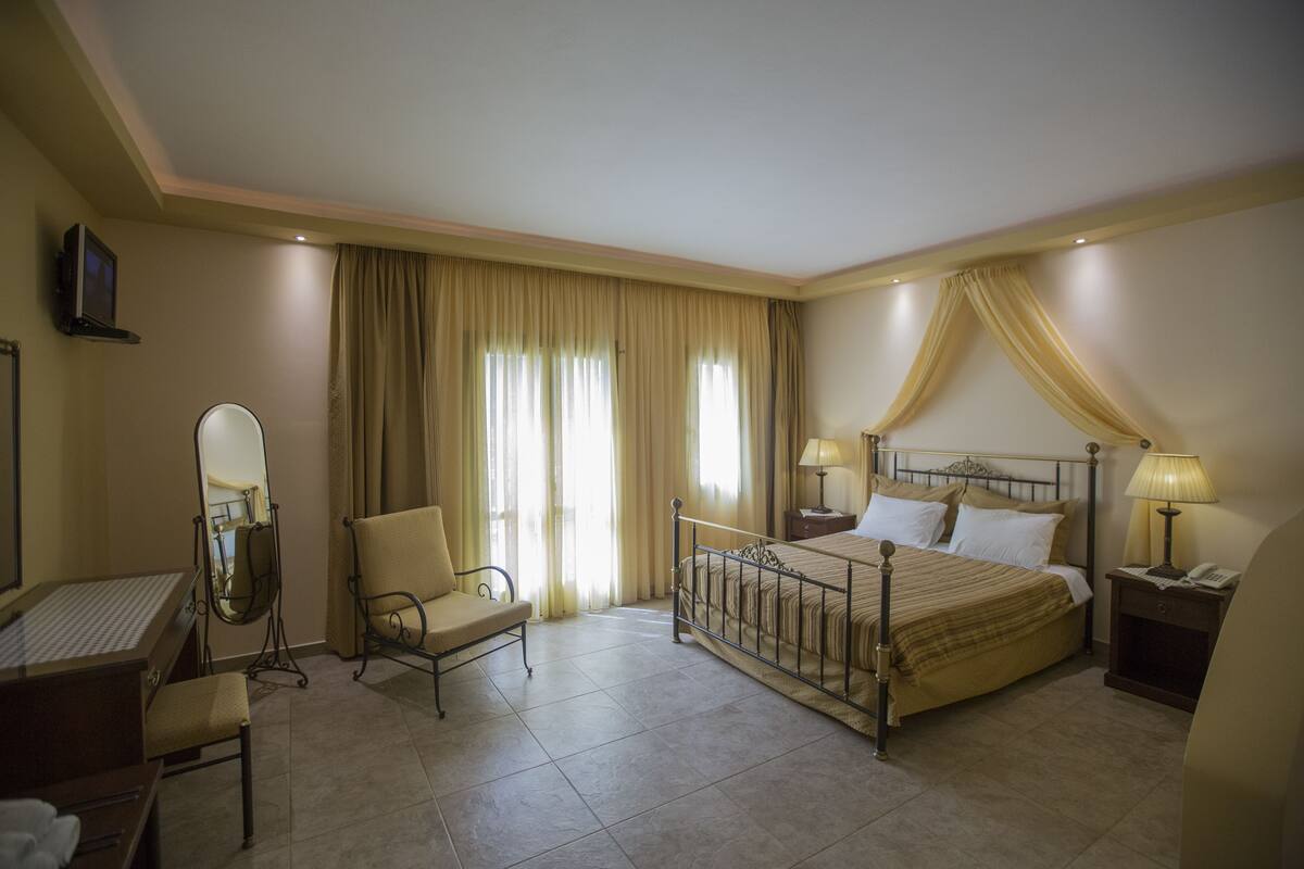A hotel room with a bed, a desk, a chair, a vanity with a mirror, and curtains.