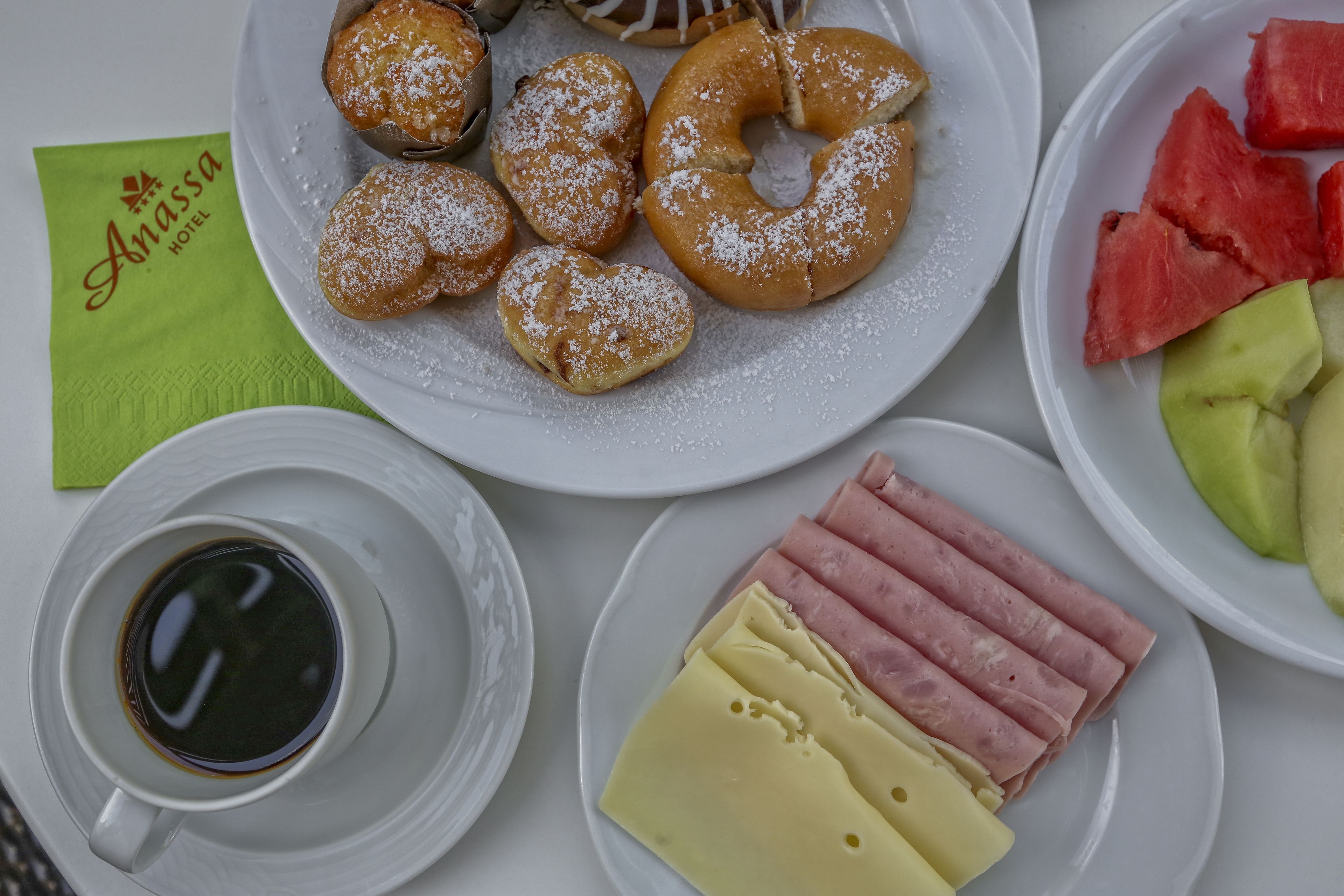 En frukosttallrik med bakverk, skinka, ost och vattenmelon.
