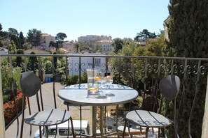 A balcony with a round table and two chairs, overlooking a residential area with buildings and trees. - Kimi Résidence (Cannes)