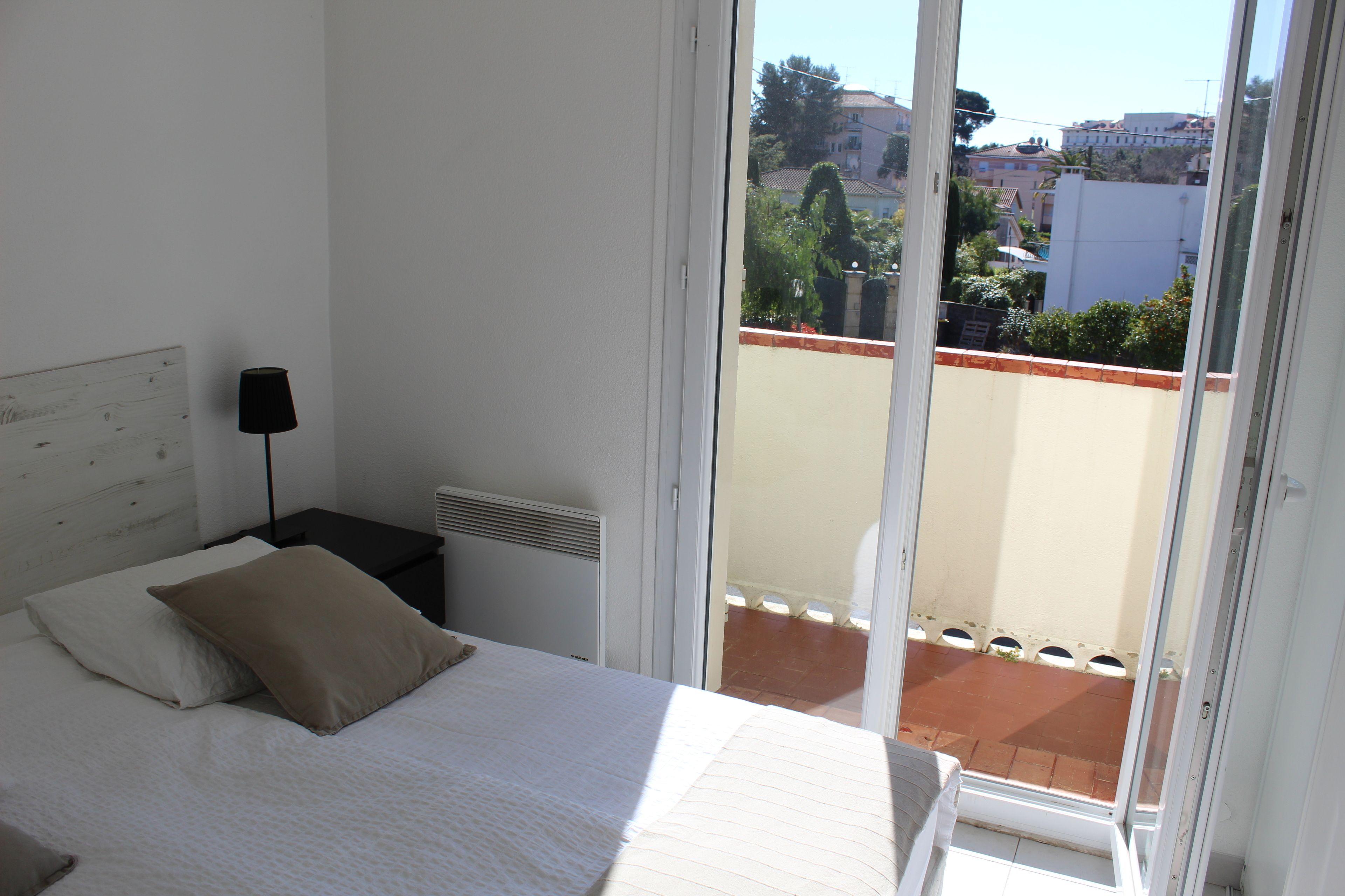 A bedroom with a bed, a nightstand, and a window with a view of buildings and trees.