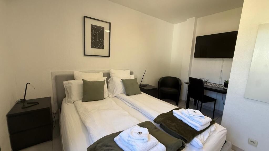 A hotel room with a bed, a desk, a chair, a TV, and a framed picture on the wall.