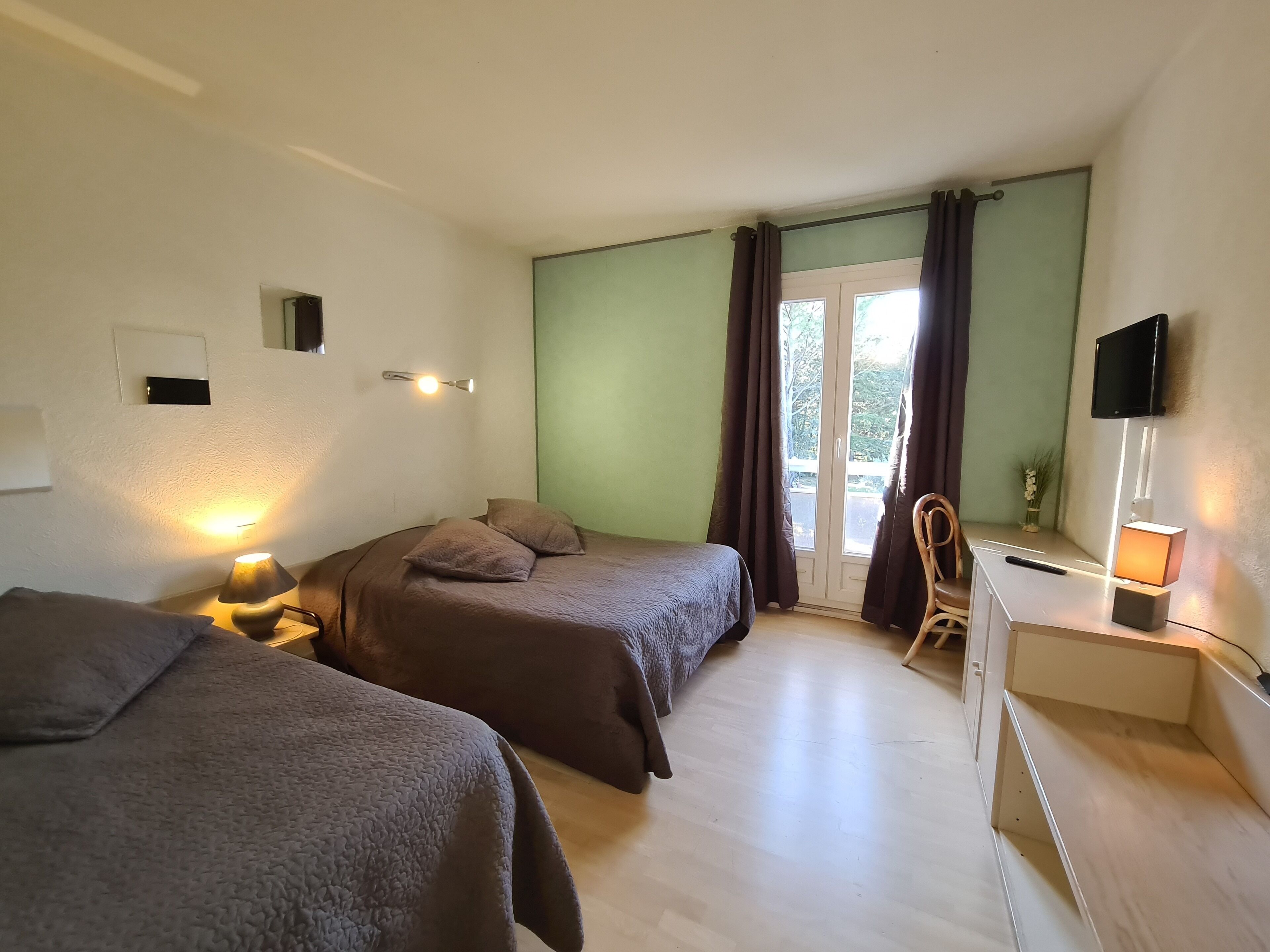 A hotel room with two beds, a desk, a chair, a TV, and a window with curtains.