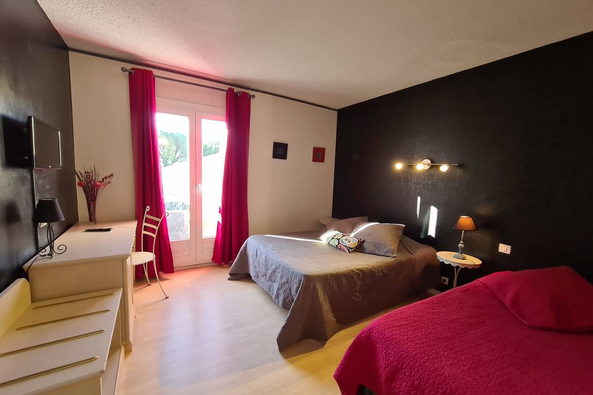A bedroom with a bed, a desk, a chair, a TV, and a window with curtains.