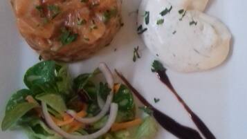 Un plato con tártara de salmón, salsa blanca, ensalada de espinacas y salsa oscura.