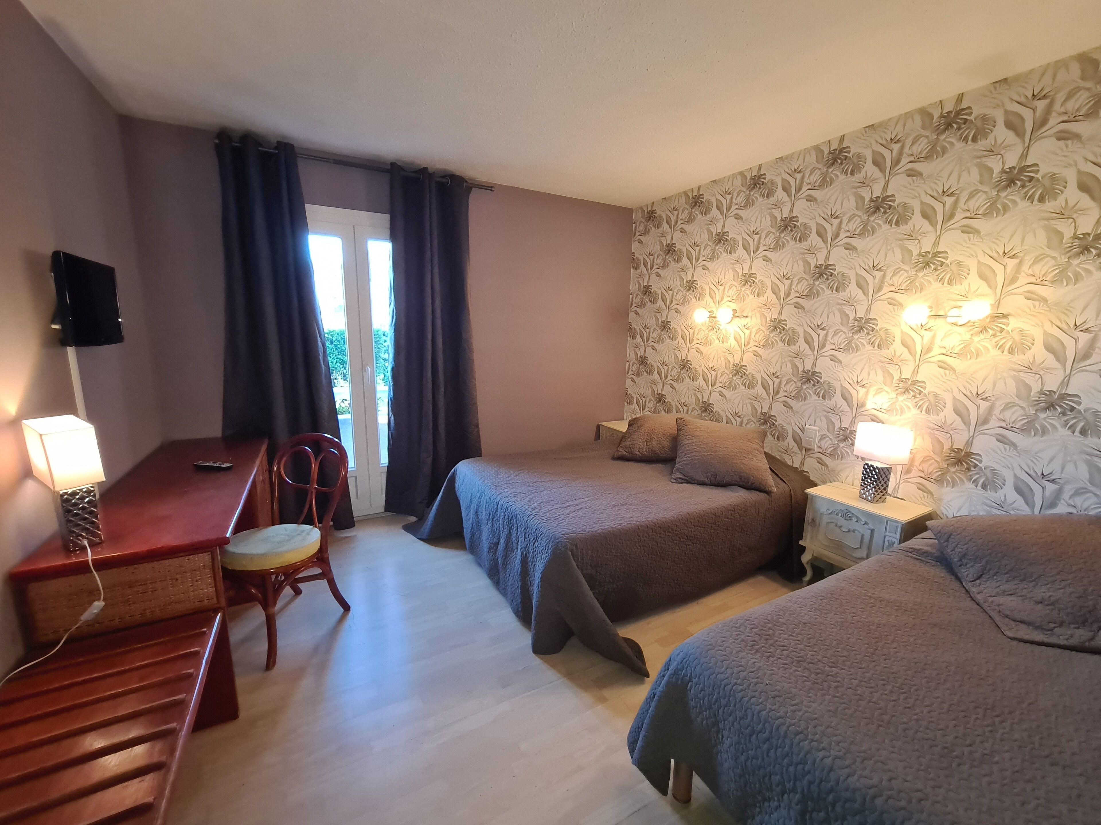 A hotel room with two beds, a desk, a chair, and a TV.