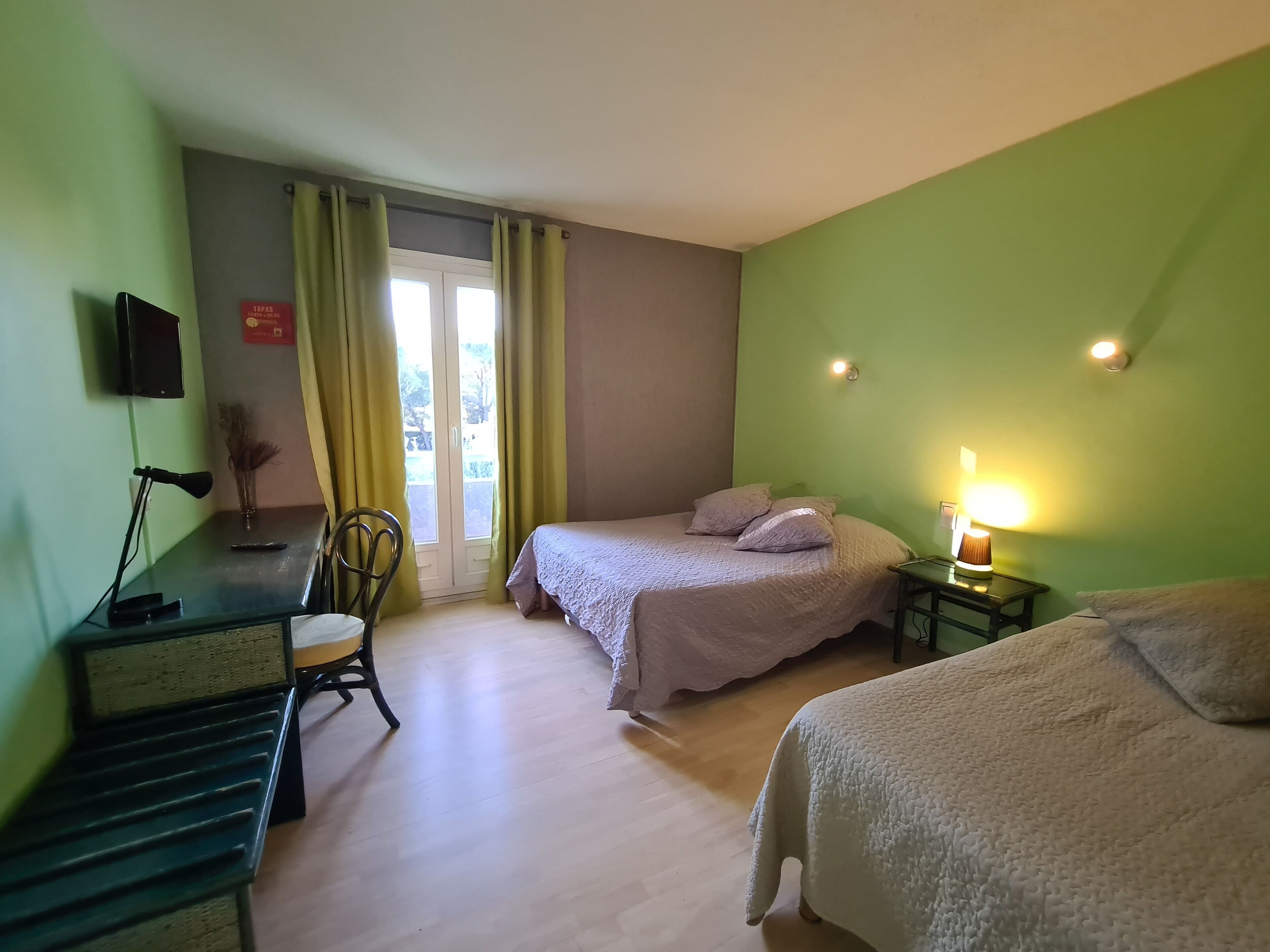 A bedroom with a bed, a desk with a lamp, a chair, and a nightstand with a lamp.