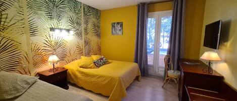 Una camera d'albergo con due letti, una scrivania, una televisione e un balcone con vista sugli alberi.