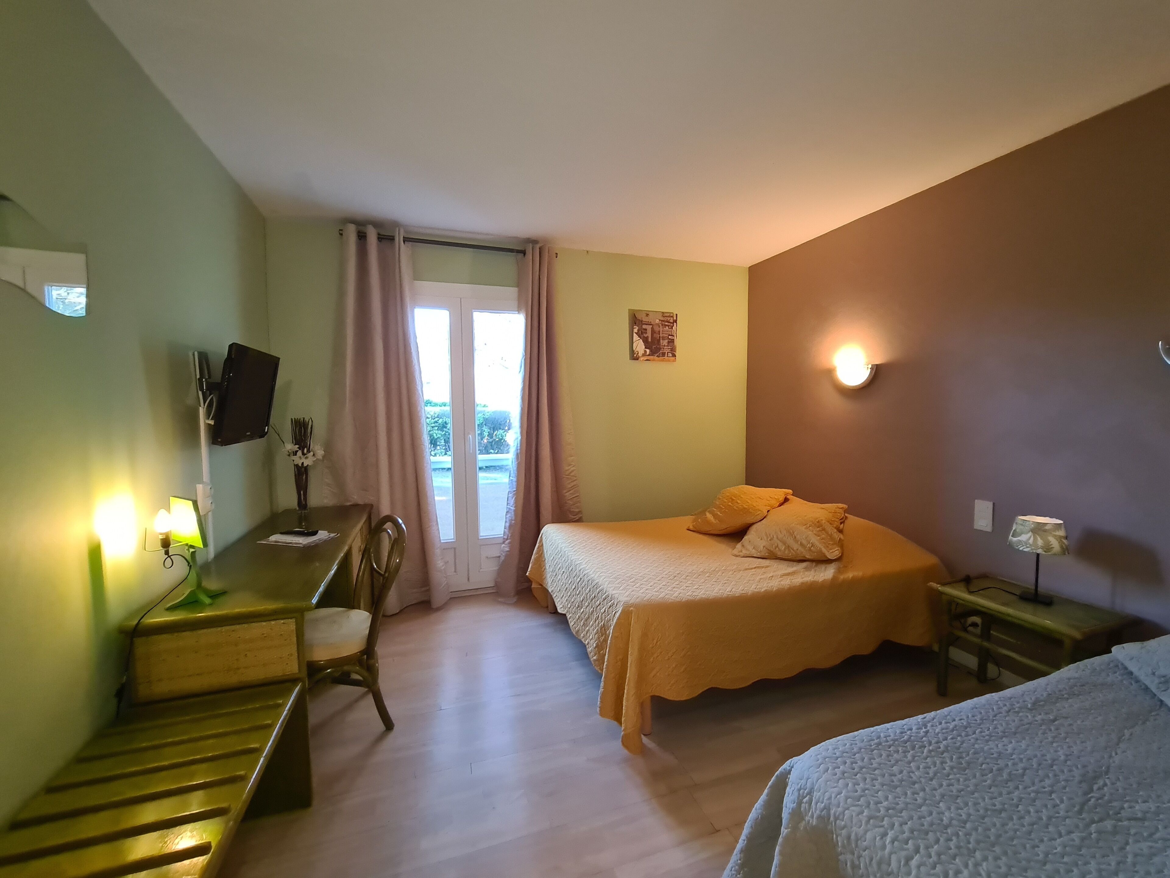 Een hotelkamer met een bed, een bureau met stoel, een aan de muur bevestigde televisie en een raam met gordijnen.