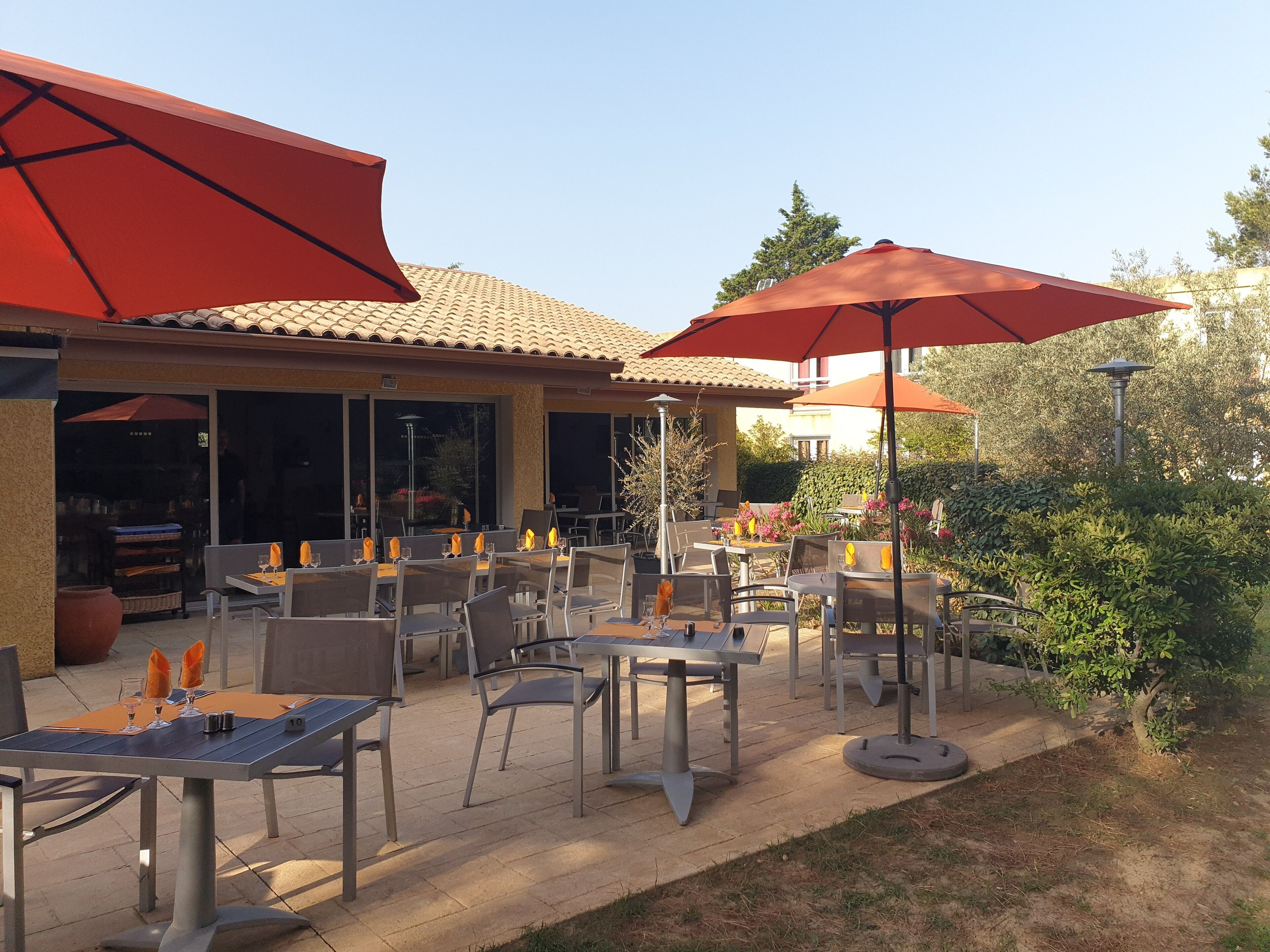 Une terrasse extérieure avec des tables et des chaises, des parasols rouges et un toit recouvert de tuiles.