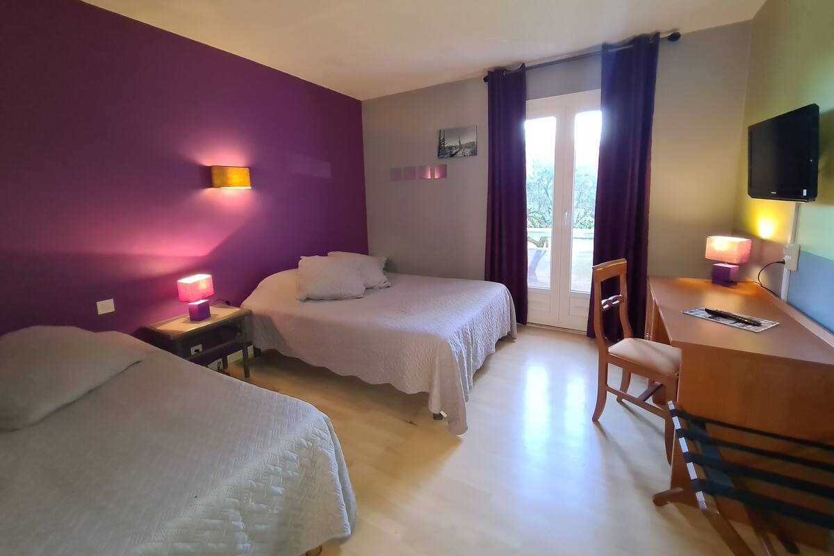 A hotel room with two beds, a desk, a chair, a television, and a window with curtains.