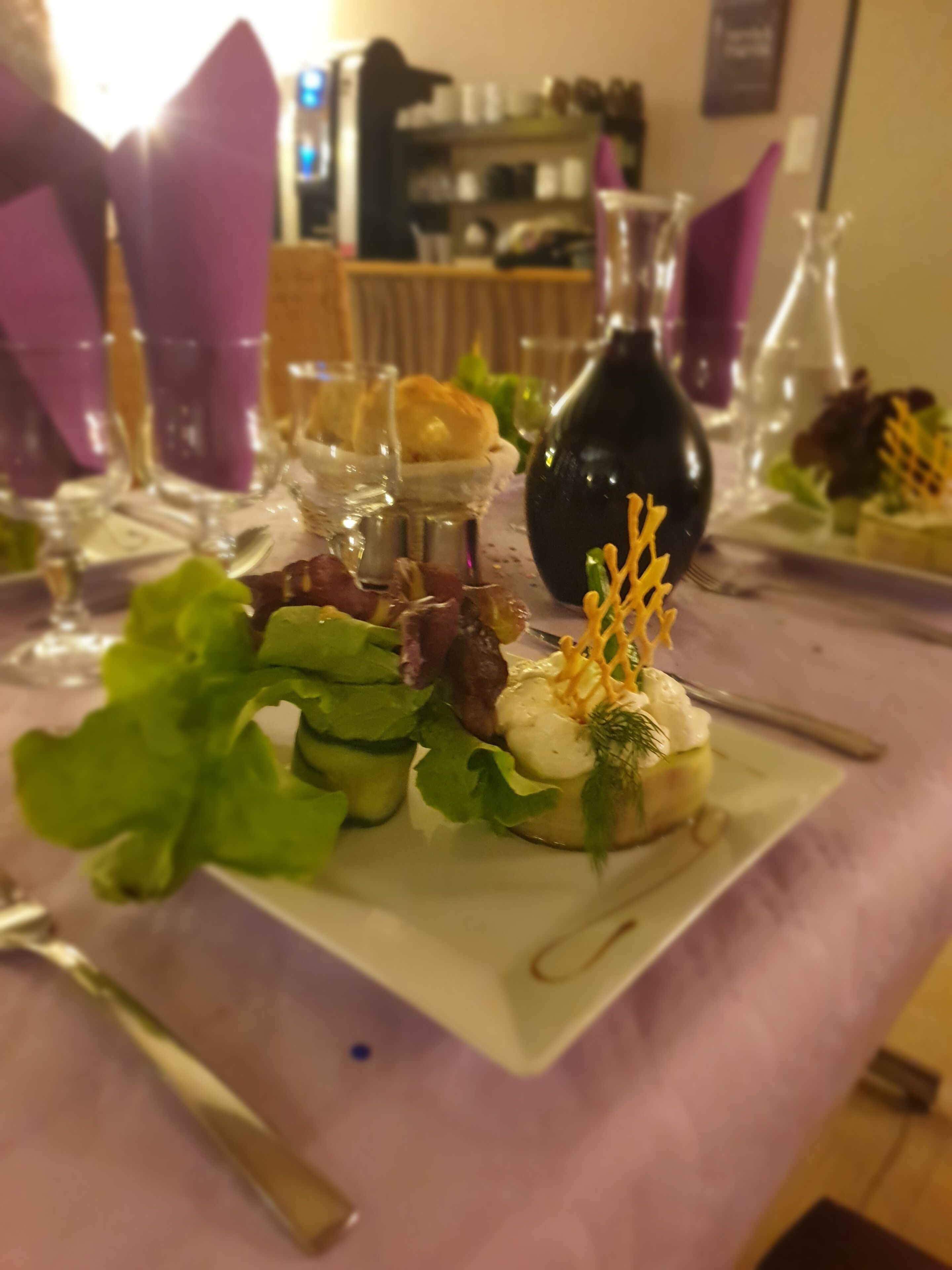 Ein Esstisch mit verschiedenen Speisen, darunter ein Salat mit Blattsalaten und weißer Soße, sowie eine Flasche Olivenöl.