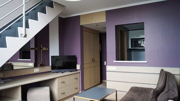 Una habitación moderna con escritorio, televisor, sofá, escalera y armario.