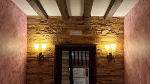 A room with exposed wooden beams, stone wall, and a mirror with two wall-mounted lights. - Hostal Ruta de Lorca (Alfacar)