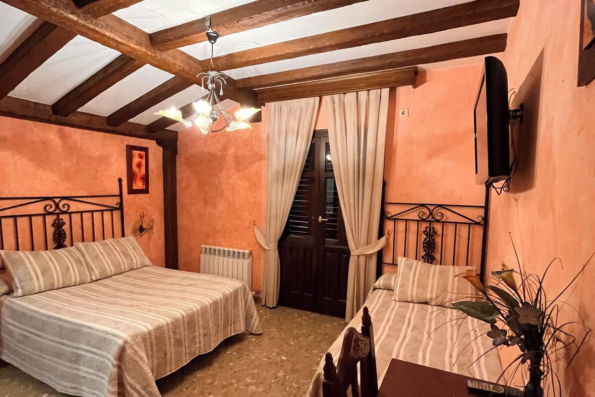 A cozy room with two beds, a wooden ceiling, a chandelier, and a small table with a vase.