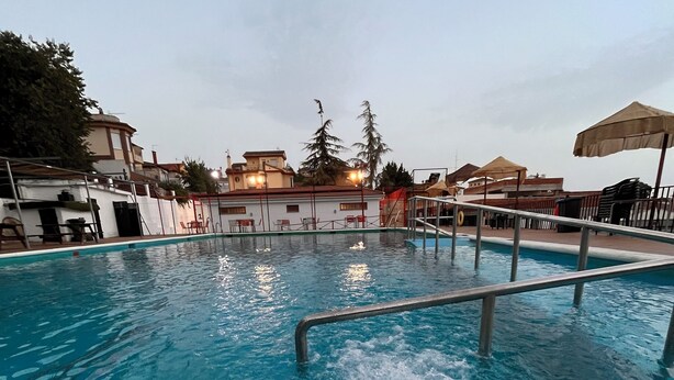 A swimming pool with a diving board, surrounded by buildings and outdoor seating. - Hostal Ruta de Lorca (Alfacar)
