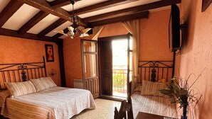 A bedroom with two beds, a wooden table, and a balcony with a view. - Hostal Ruta de Lorca (Alfacar)