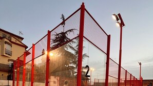 An outdoor tennis court with red fencing and floodlights. - Hostal Ruta de Lorca (Alfacar)