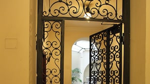 An open wrought iron gate leading to a hallway with a tiled floor and a potted plant in the background. - La Maison dell'Orologio (Rome)