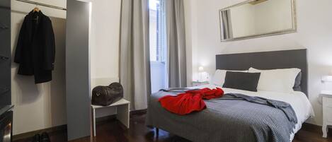 A bedroom with a bed, a mirror, a wardrobe, a nightstand, and a window with curtains.