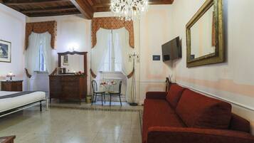 A room with a bed, a red sofa, a wooden dresser, a table with chairs, a chandelier, and a large mirror on the wall.