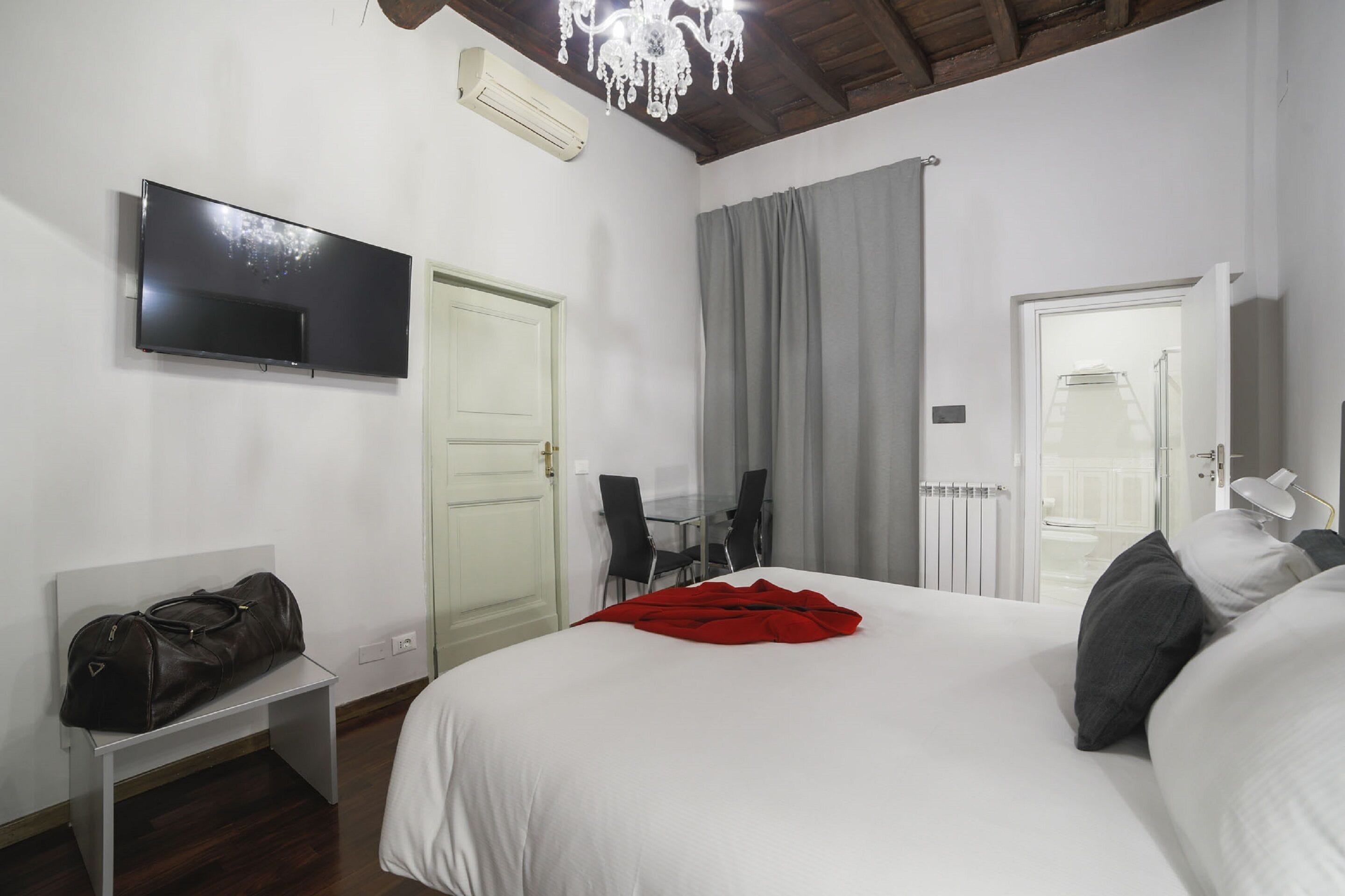 Ein Hotelzimmer mit Bett, Wandfernseher, Schreibtisch mit Stuhl und einem Fenster mit Vorhängen.