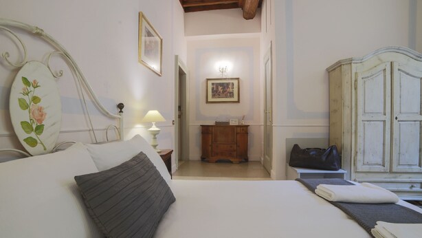 A bedroom with a bed, bedside table, lamp, wardrobe, and a hallway leading to a bathroom. - La Maison dell'Orologio (Rome)
