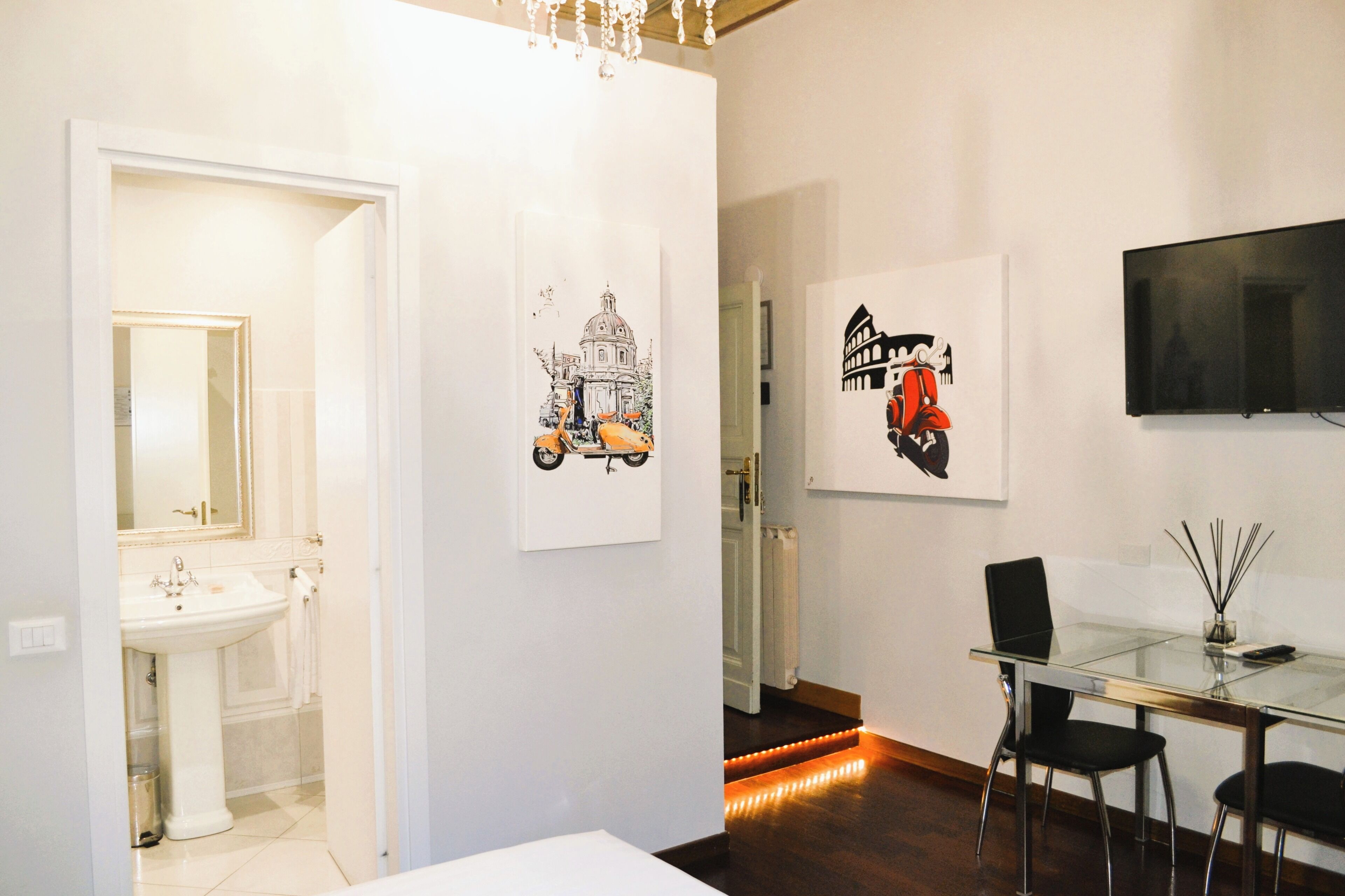Een moderne hotelkamer met een glazen eettafel, zwarte stoelen, een witte wastafel en kunstwerken aan de muur.