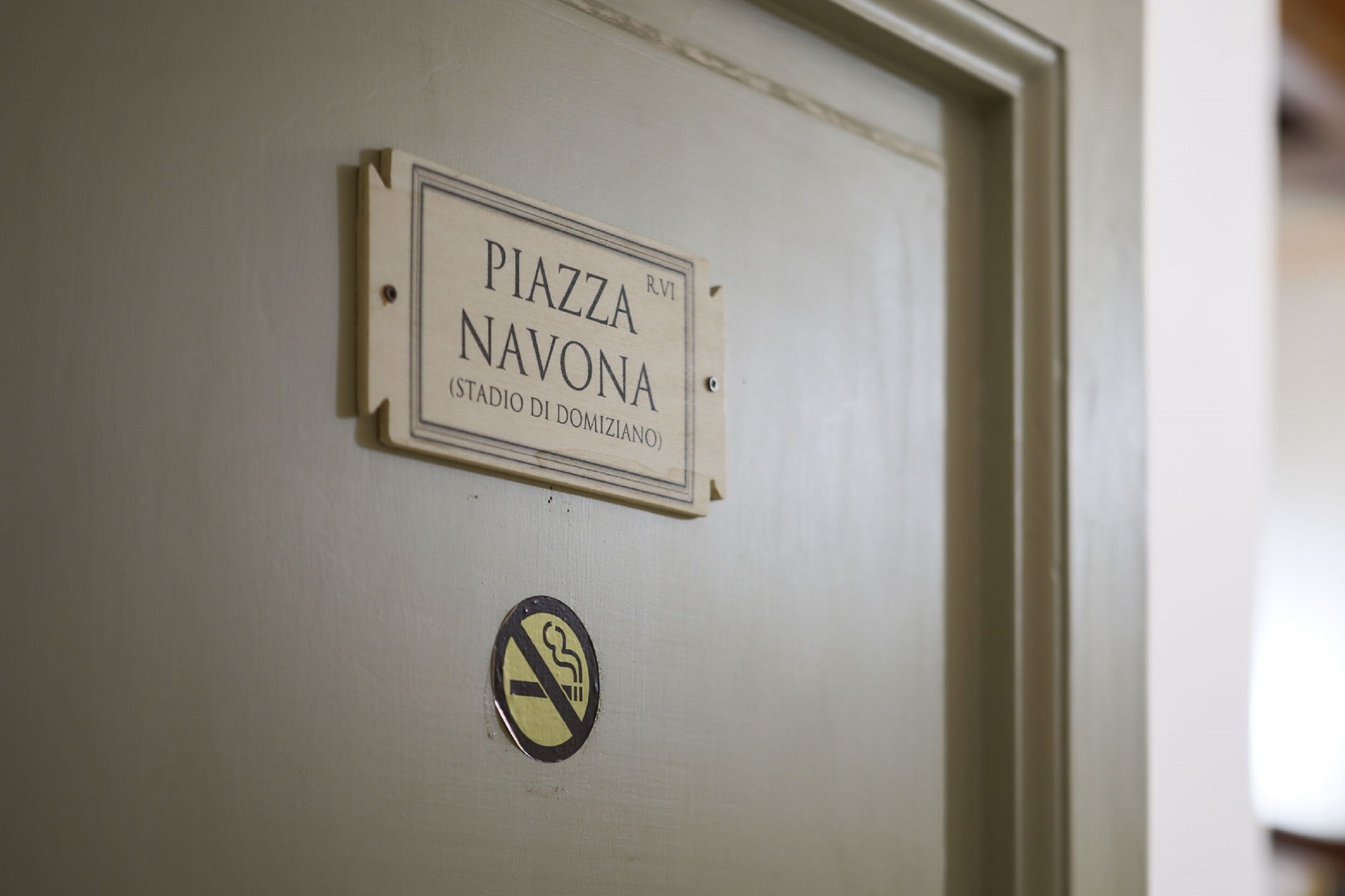 Una puerta con un cartel que dice "PIAZZA NAVONA (STADIO DI DOMIZIANO)" y un letrero de prohibido fumar.