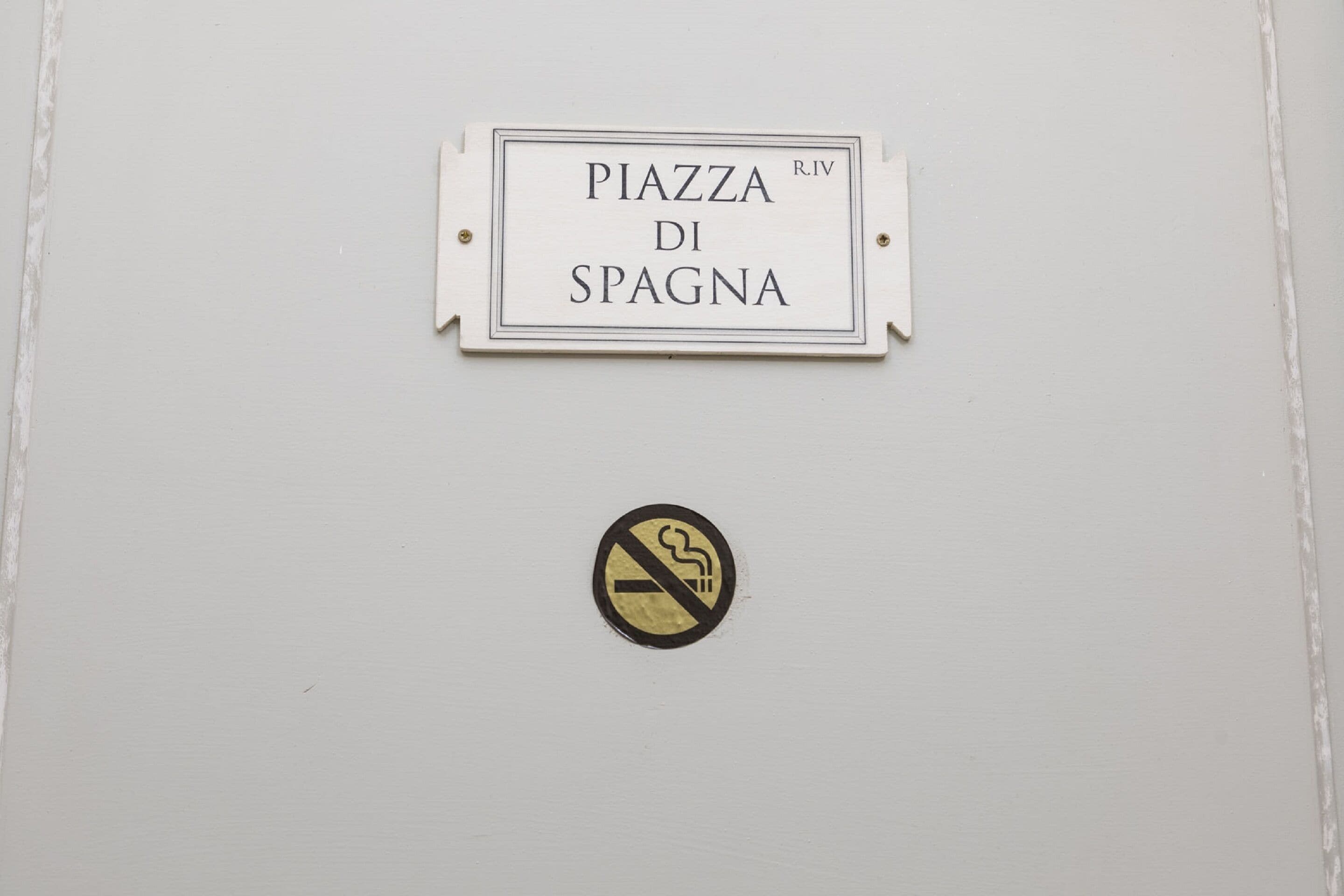 Un panneau indiquant « PIAZZA DI SPAGNA » avec un symbole interdisant de fumer en dessous.
