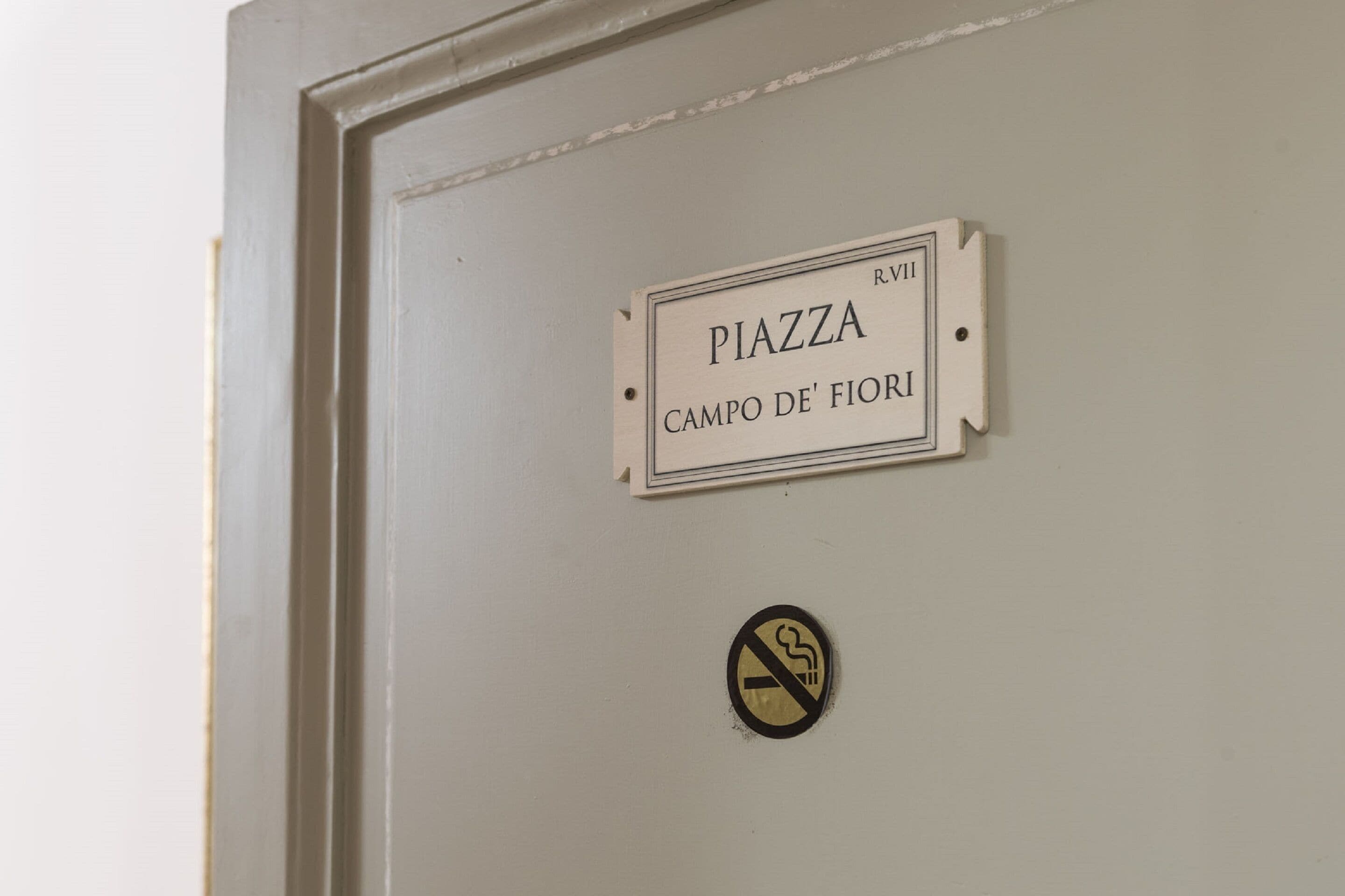 Una puerta con un letrero que dice "PIAZZA CAMPO DE' FIORI" y un cartel de prohibido fumar debajo.