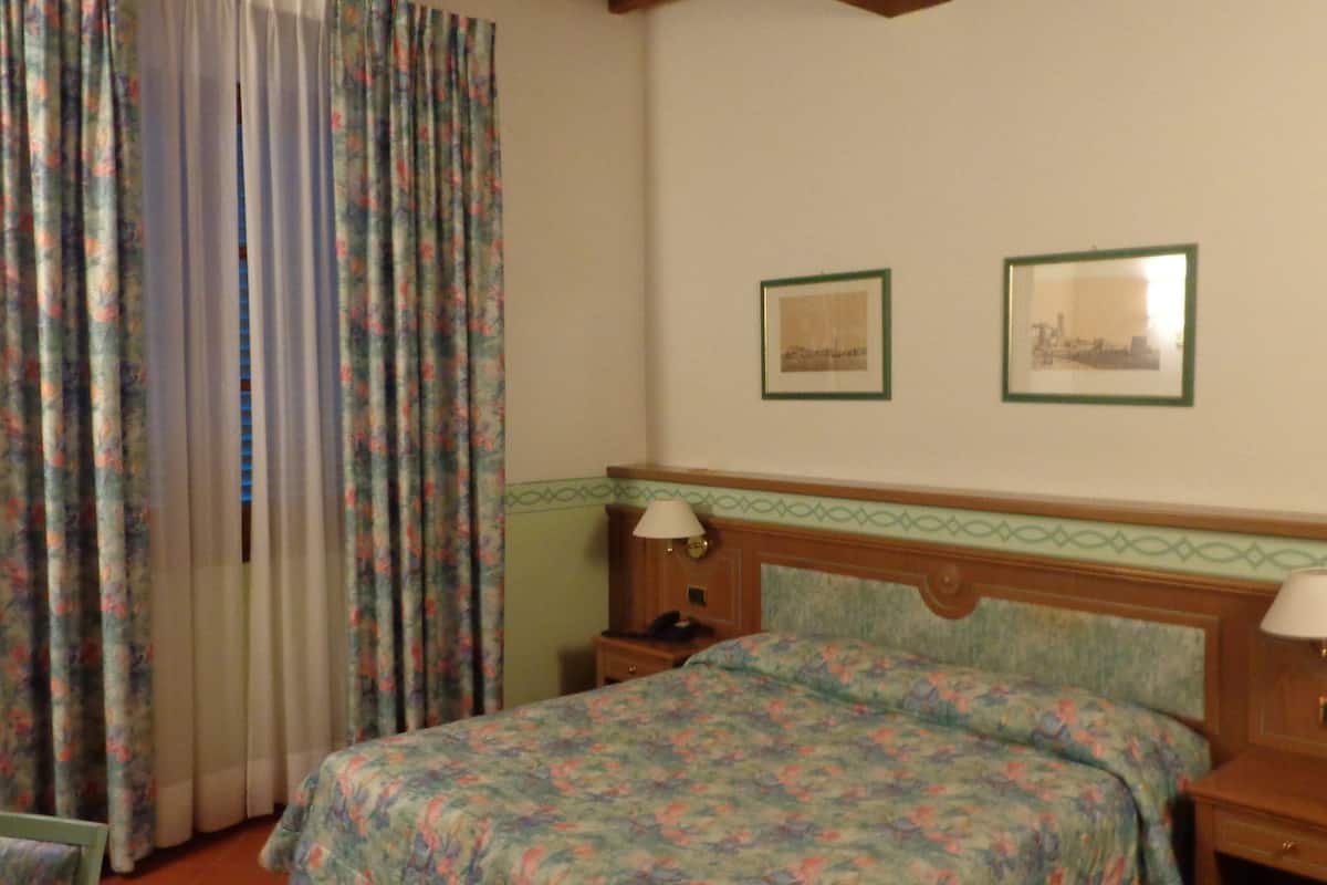 Een slaapkamer met een bloemenbedekker, twee nachtkastjes met lampen, en drie ingelijste foto’s aan de muur.