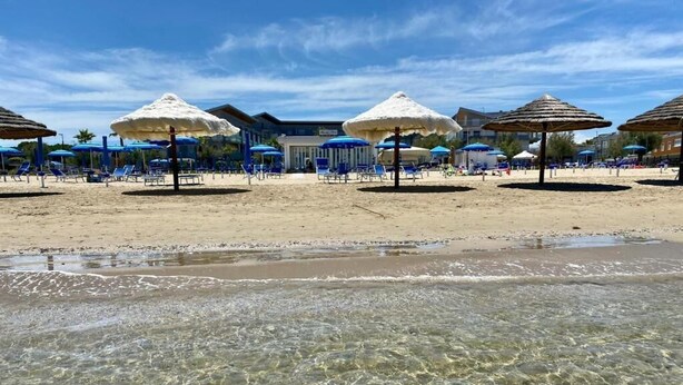 En strand med klart, grunt vatten, parasoller och solstolar.