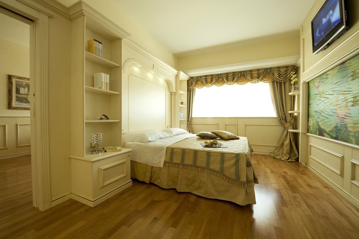 A bedroom with a bed, bedside tables, a TV, and a window with curtains.