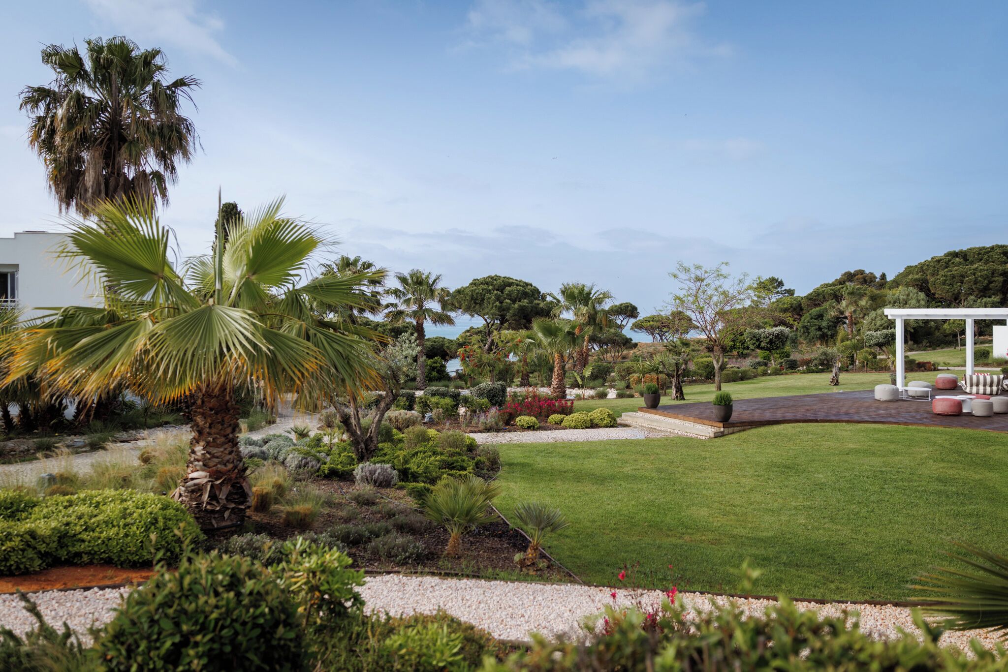 A well-maintained garden with palm trees, a white gazebo, and a clear sky.