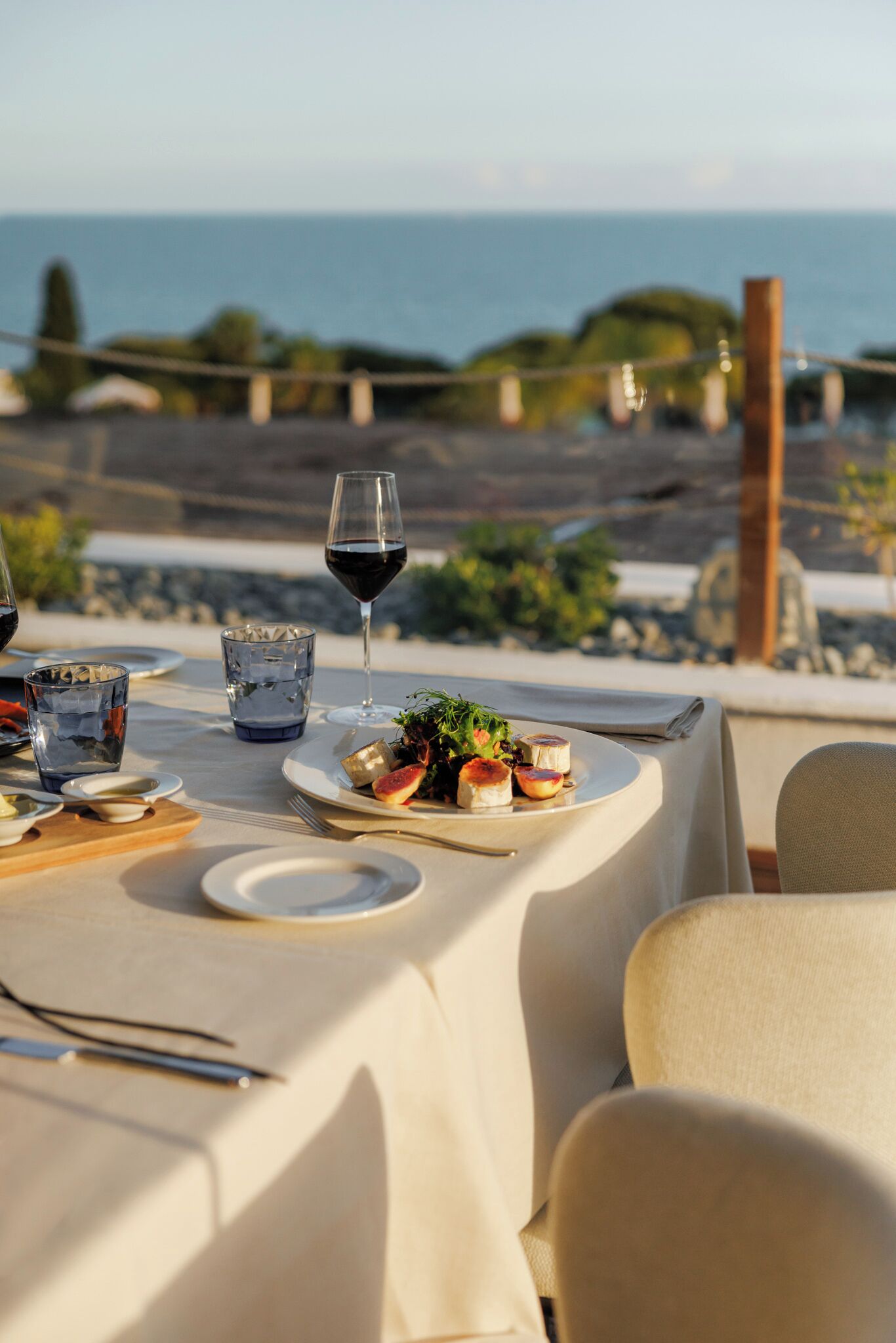 A table set for a meal with a view of the sea and rocky landscape.
