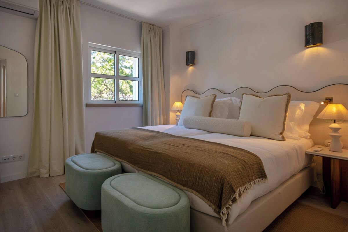 A bedroom with a bed, two bedside lamps, a window, and a mirror.