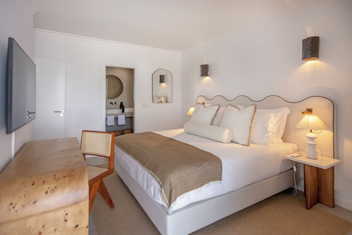 Une chambre à coucher comprenant un lit, une table de chevet, une lampe, une chaise et un téléviseur fixé au mur.