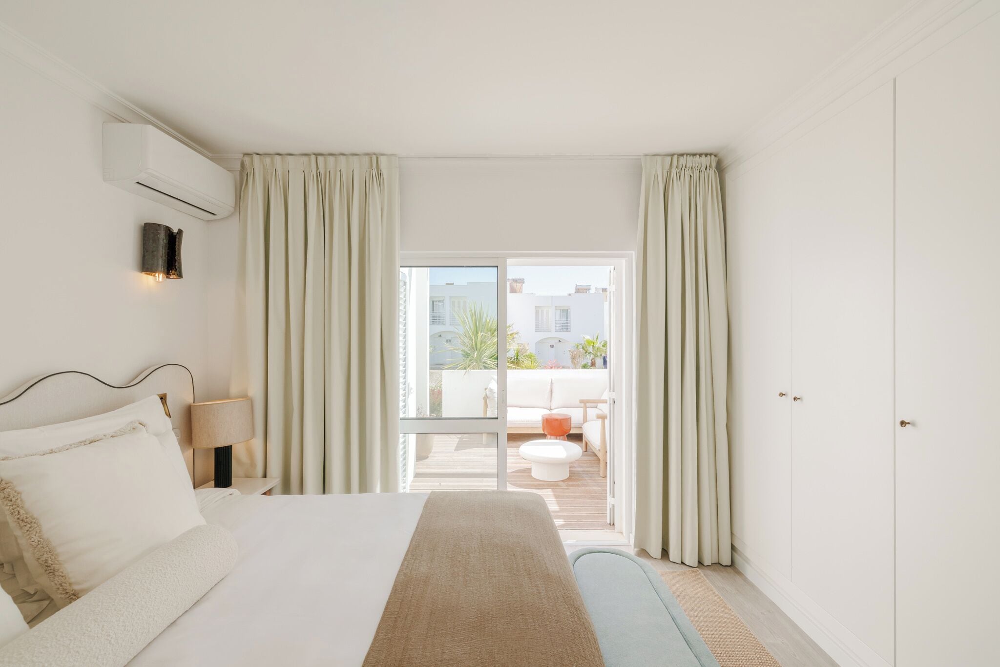 Ein Hotelzimmer mit Bett, Nachttisch, Klimaanlage, Lampe und Blick auf einen Balkon.