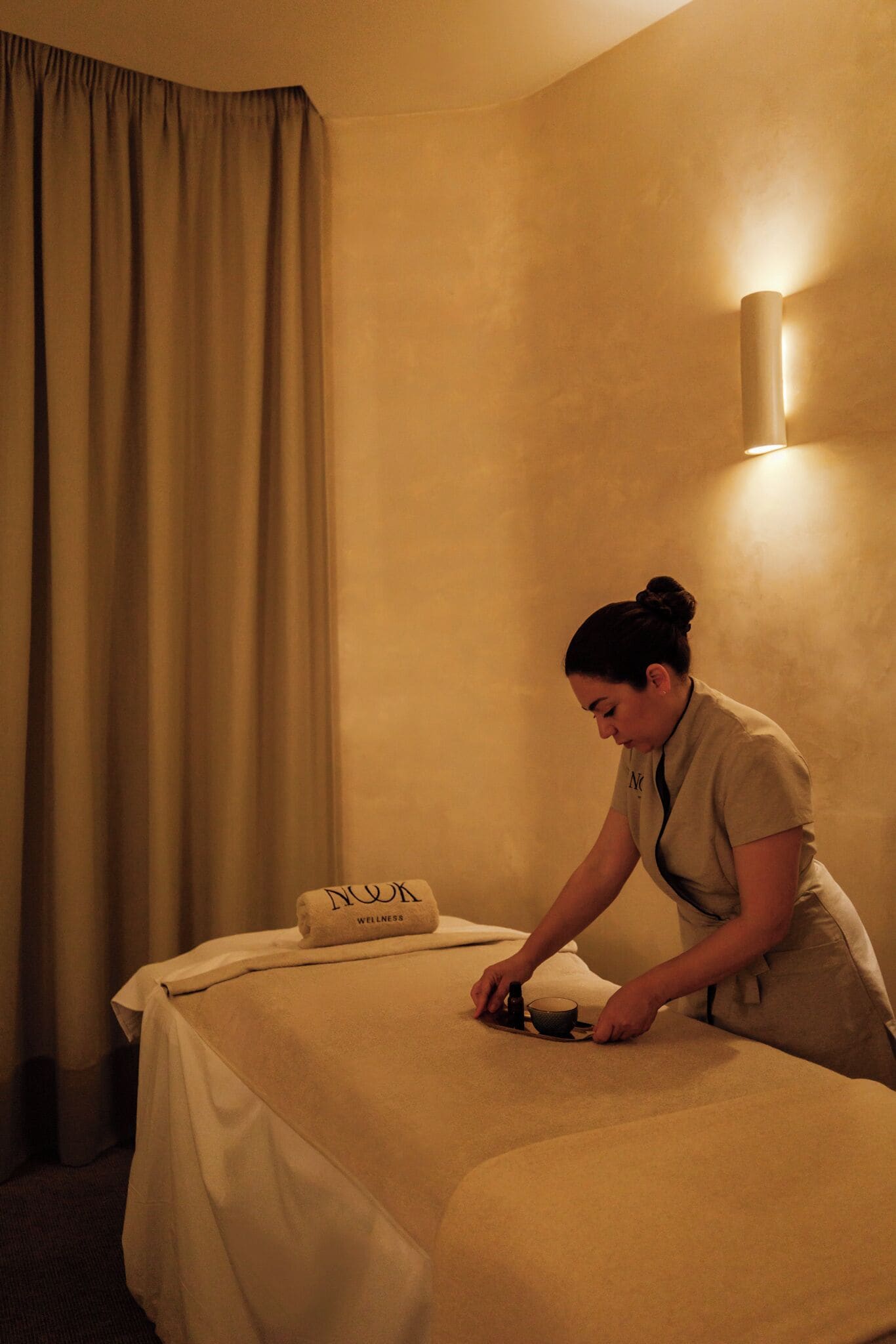 A room with a bed, a towel, and a wall-mounted light fixture.