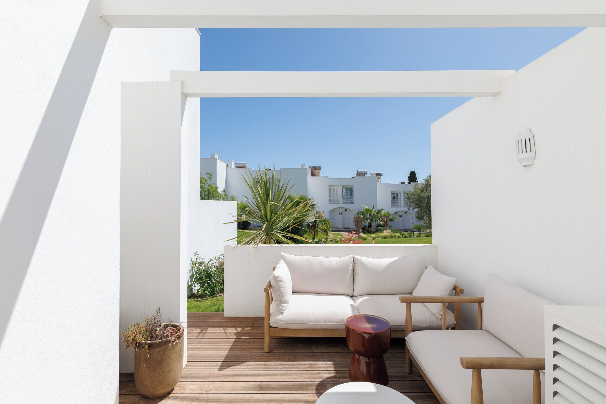A balcony with a white sofa, a wooden table, and a potted plant.