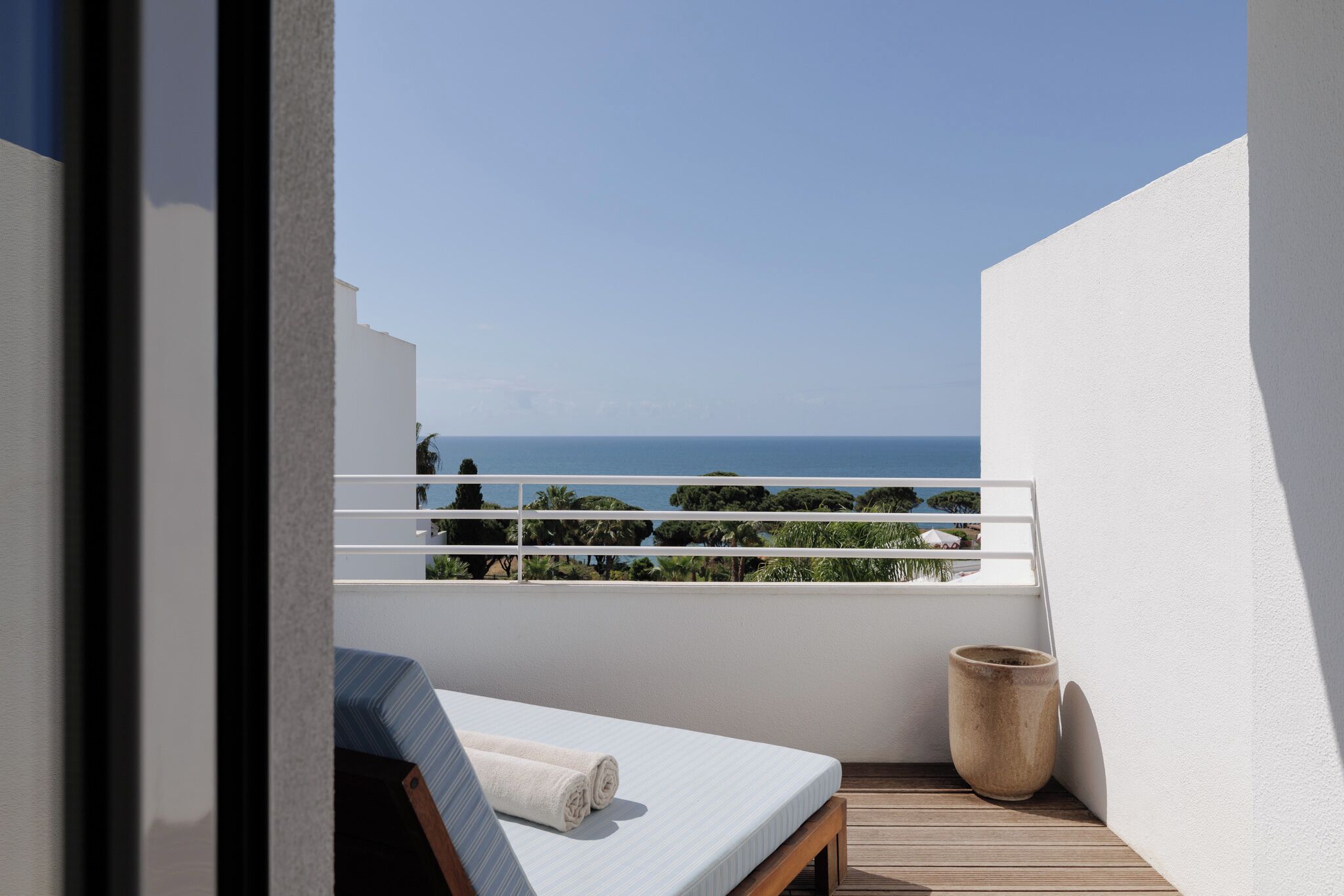 Un balcón con una cama, una planta en maceta y vista al mar.