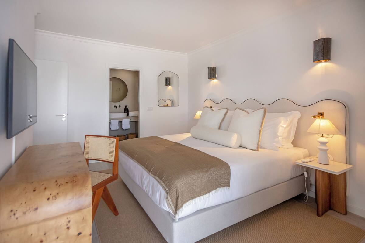 A bedroom with a bed, bedside table, lamp, chair, and a TV mounted on the wall.